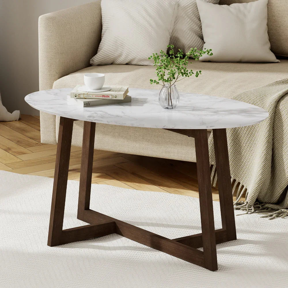Modern oval coffee table with white marble top and wood base in a cozy living room setting
